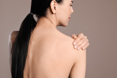 Woman suffering from shoulder pain on beige background, closeup