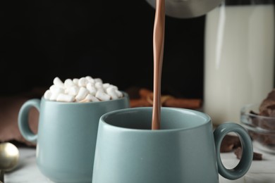 Photo of Pouring hot cocoa drink into cup on black background, closeup