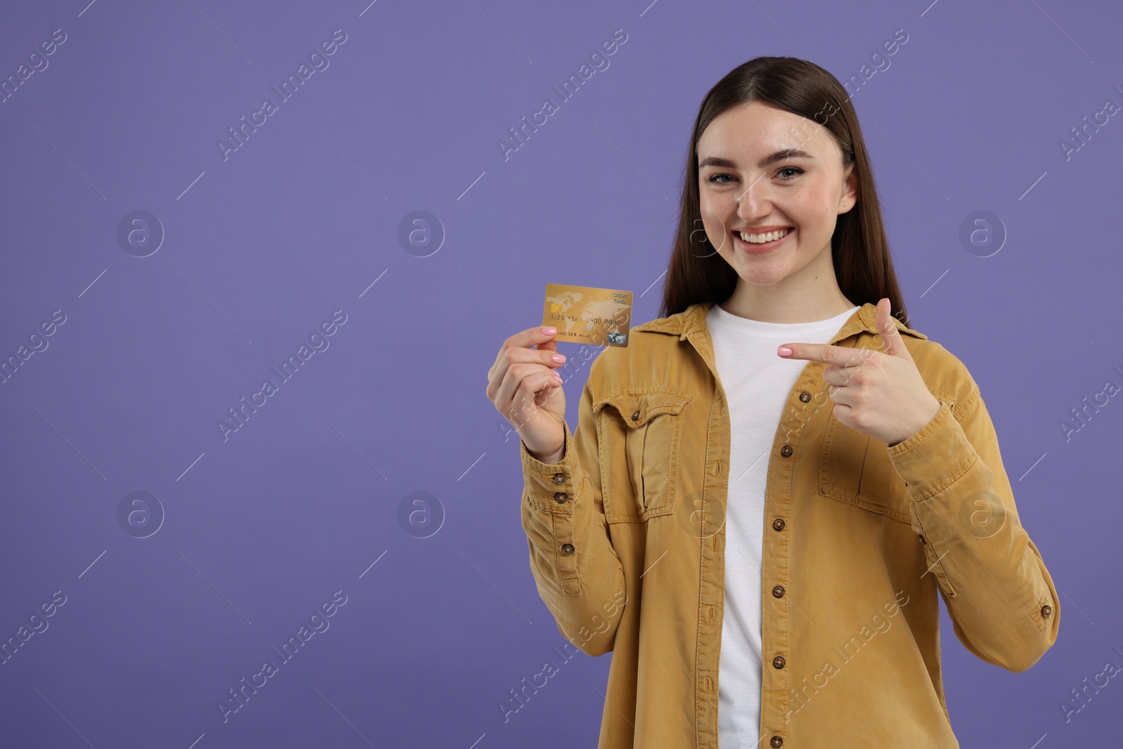 Photo of Happy woman pointing at credit card on purple background, space for text