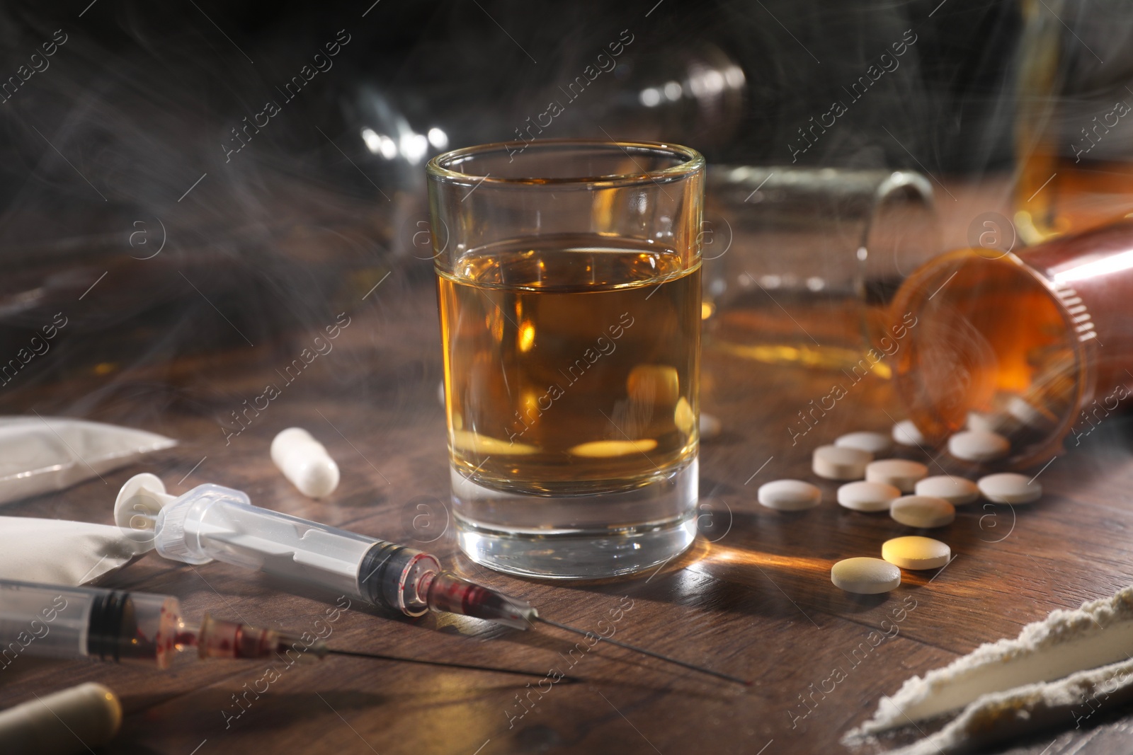 Photo of Alcohol and drug addiction. Whiskey in glass, syringes, pills and cocaine on wooden table