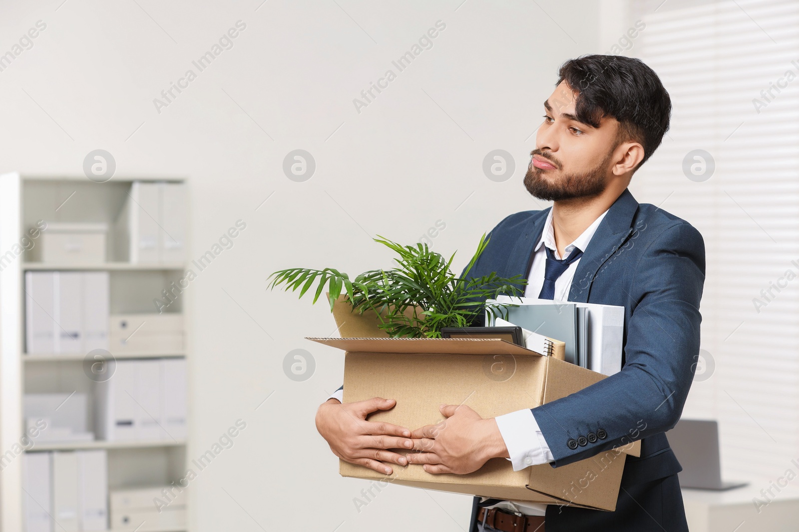 Photo of Unemployment problem. Frustrated man with box of personal belongings in office