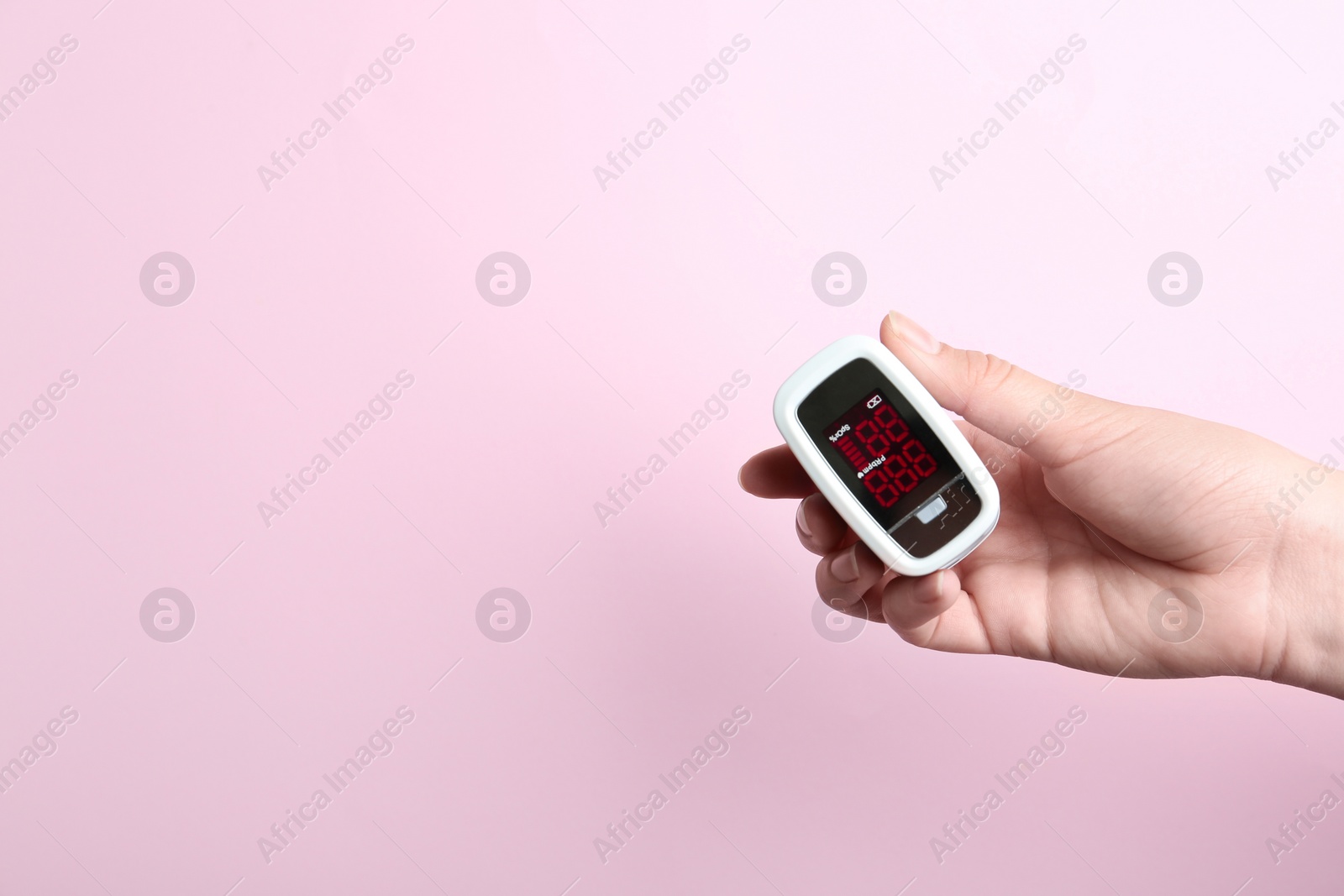 Photo of Woman holding fingertip pulse oximeter on pink background, closeup. Space for text