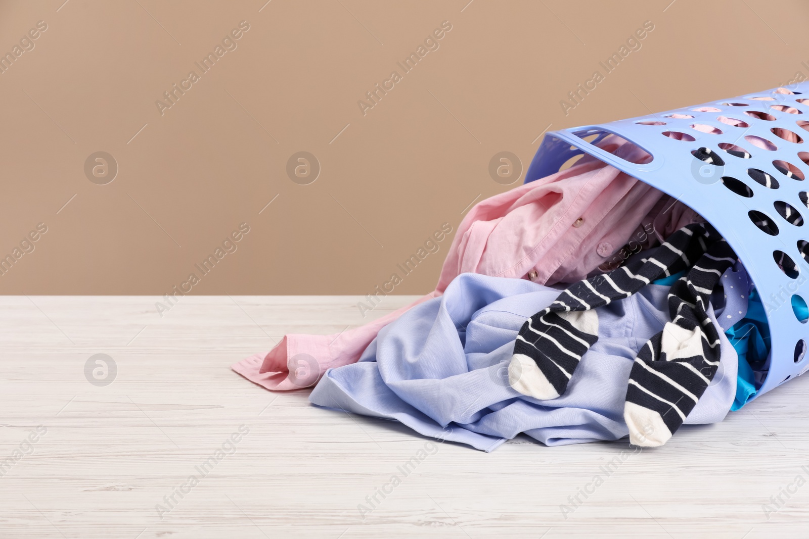 Photo of Plastic laundry basket with clothes near beige wall. Space for text