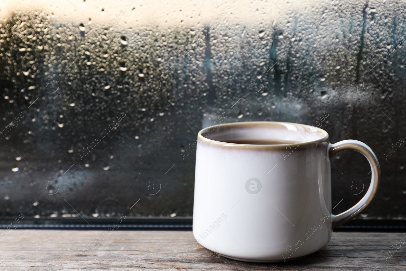 Photo of Cup of hot tea on wooden window sill. space for text. Rainy weather