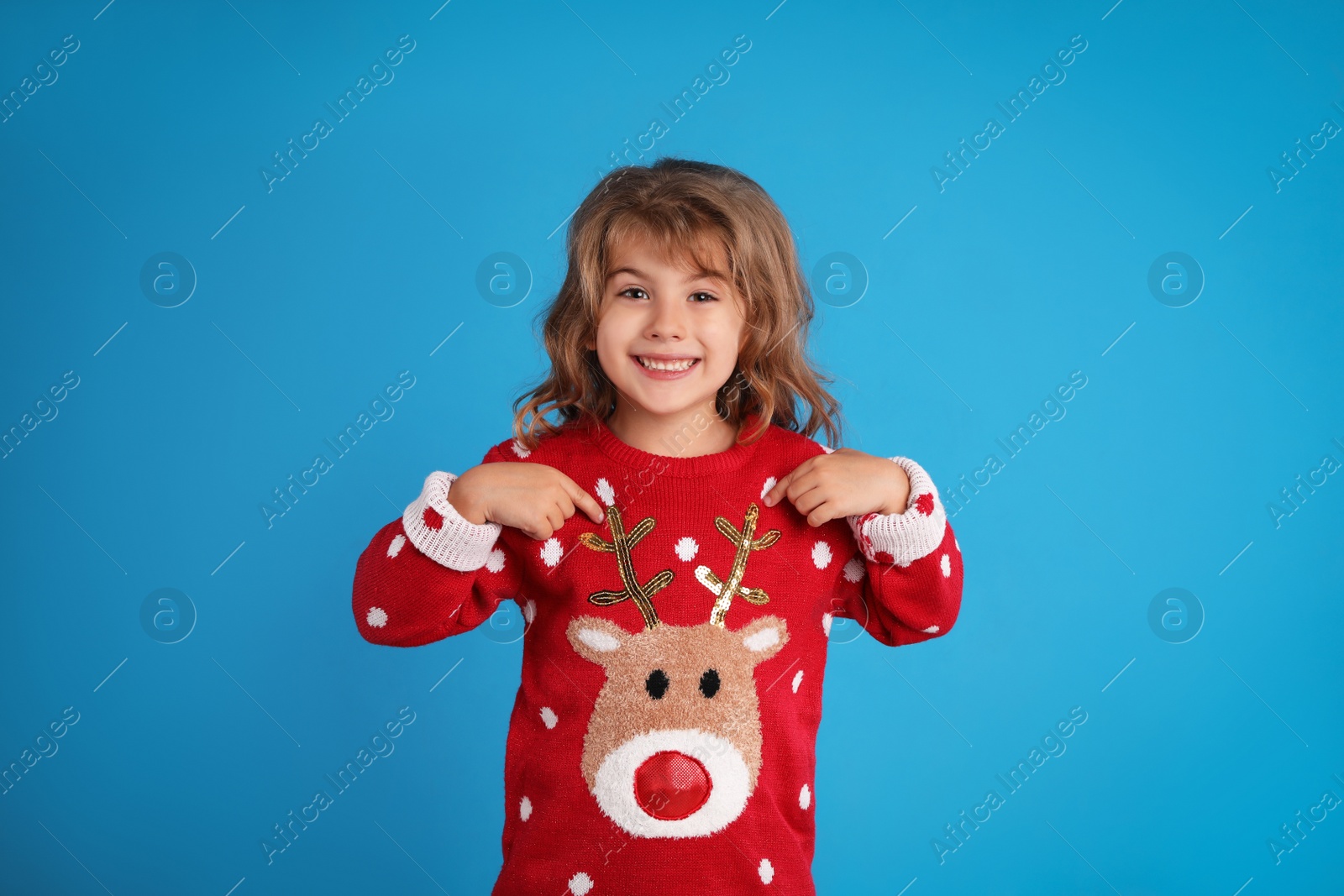 Photo of Cute little girl pointing at her red Christmas sweater against blue background