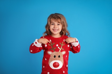 Cute little girl pointing at her red Christmas sweater against blue background