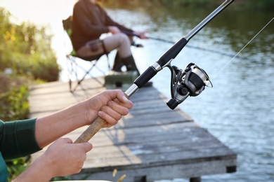 Photo of Man with rod fishing on wooden pier at riverside. Recreational activity