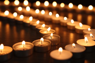 Photo of Burning candles on wooden table in darkness, closeup