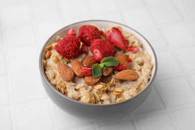 Delicious oatmeal with freeze dried strawberries, almonds and mint on white tiled table, closeup