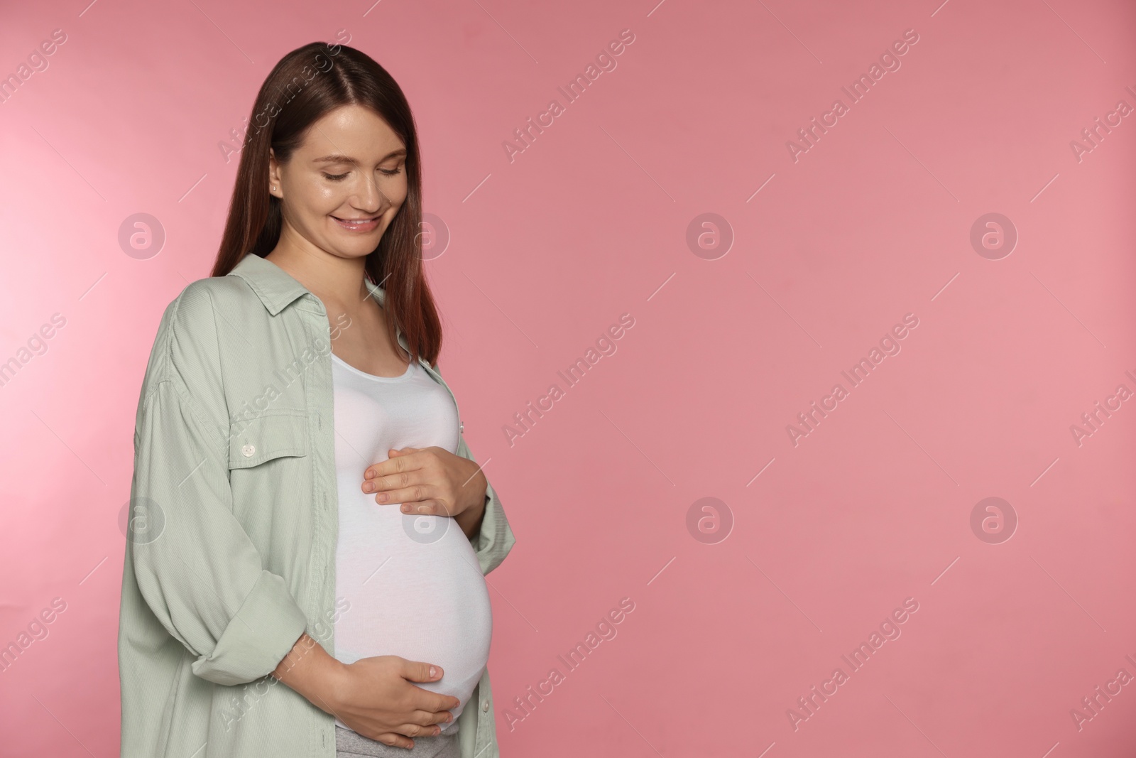 Photo of Happy young pregnant woman on pink background. Space for text