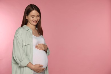 Happy young pregnant woman on pink background. Space for text