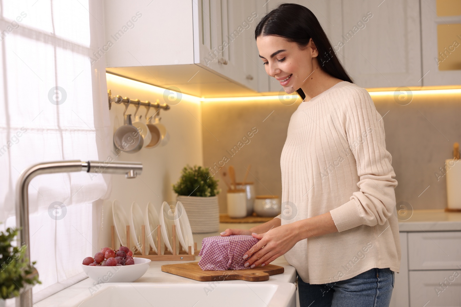 Photo of Happy woman packing bowl into beeswax food wrap at countertop in kitchen