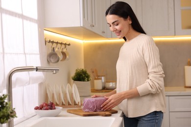 Happy woman packing bowl into beeswax food wrap at countertop in kitchen