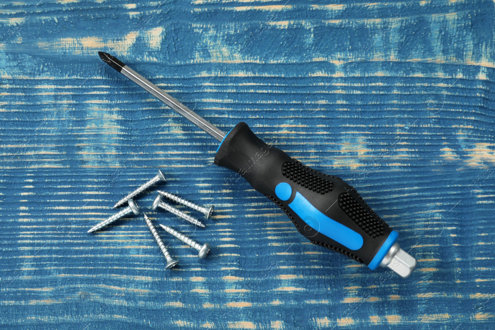 Photo of Screwdriver with black handle and screws on blue wooden table, flat lay