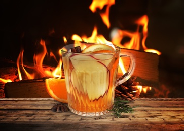 Image of Mulled wine in glass cup on wooden table near fireplace