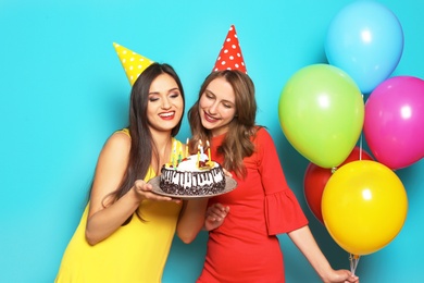 Photo of Young women with birthday cake and bright balloons on color background