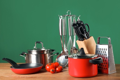 Set of clean cookware and utensils on table against color background