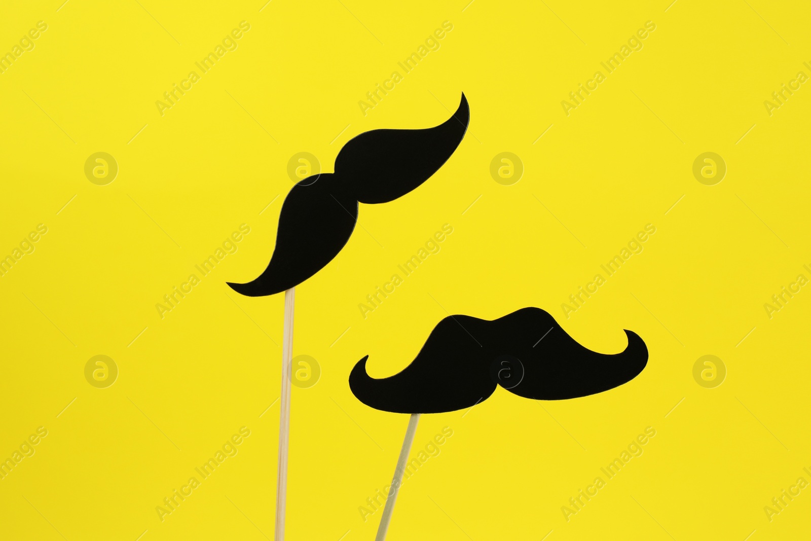 Photo of Fake paper mustaches on sticks against yellow background