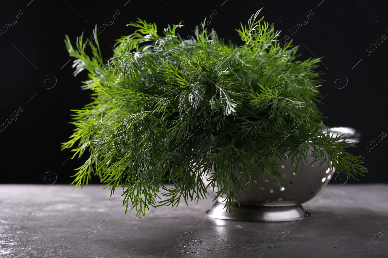 Photo of Fresh wet dill in colander on grey textured table against black background, closeup