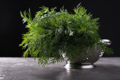 Photo of Fresh wet dill in colander on grey textured table against black background, closeup