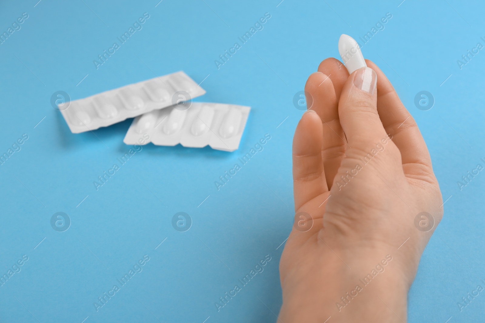 Photo of Woman holding suppository on light blue background, closeup. Hemorrhoid treatment