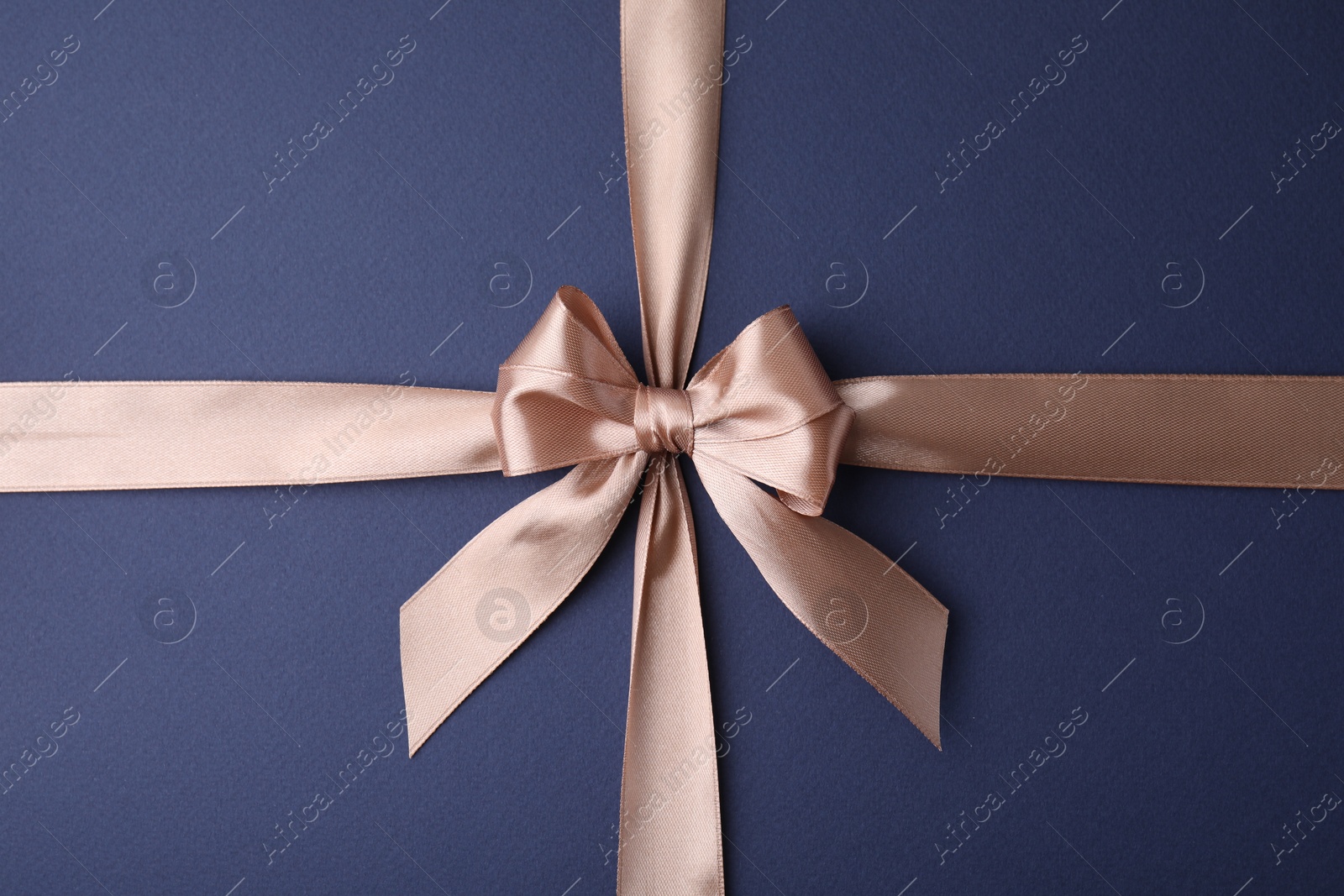 Photo of Beige satin ribbon with bow on blue background, top view