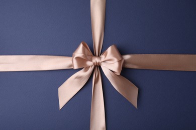 Beige satin ribbon with bow on blue background, top view