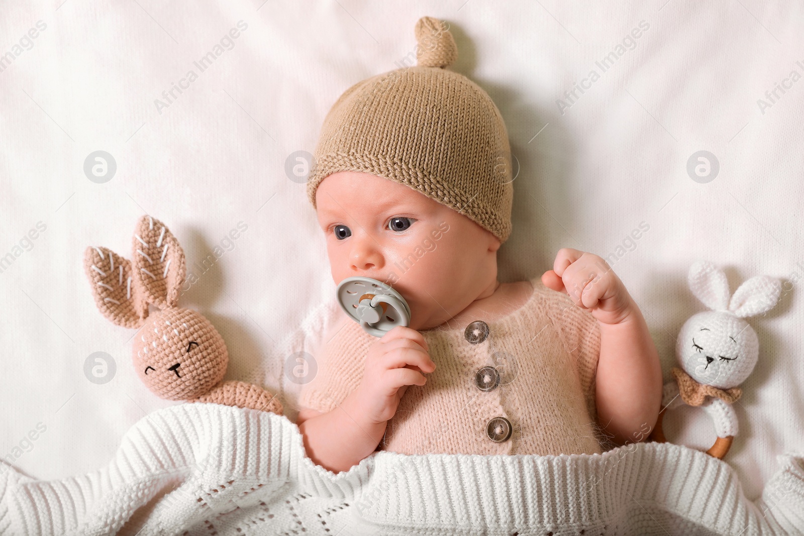 Photo of Cute newborn baby with pacifier and toys on white knitted plaid, top view