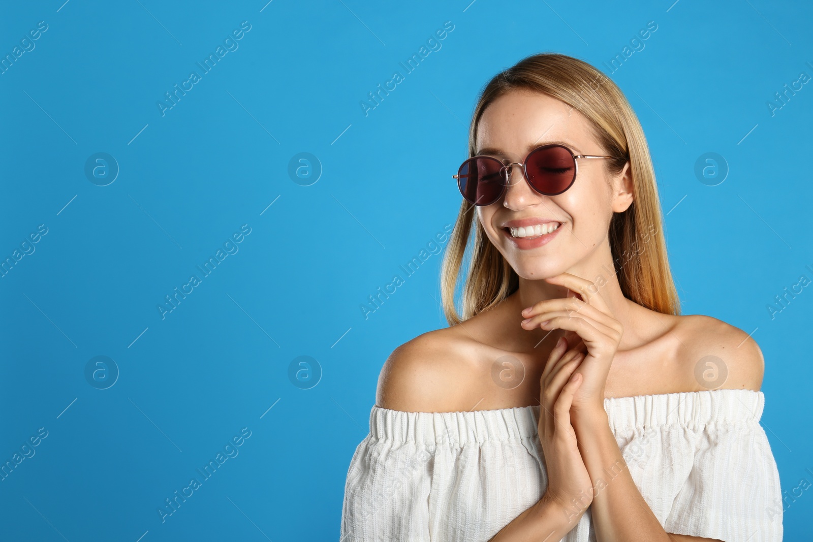 Photo of Beautiful woman in stylish sunglasses on light blue background, space for text