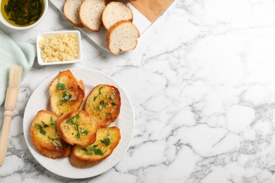 Slices of delicious toasted bread with garlic and herbs on white marble table, flat lay. Space for text