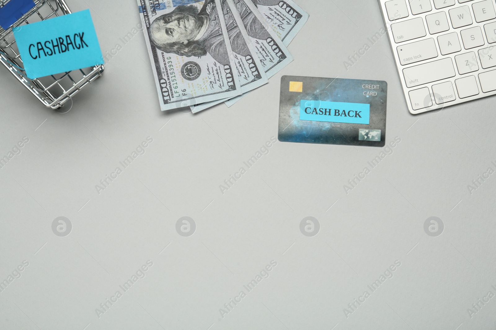 Photo of Keyboard, credit card, dollar banknotes and shopping cart on light grey background, flat lay with space for text. Cashback concept