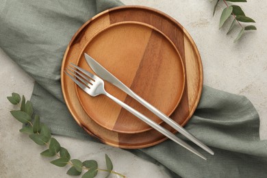 Photo of Stylish setting with cutlery, napkin, eucalyptus branches and plates on light table, flat lay