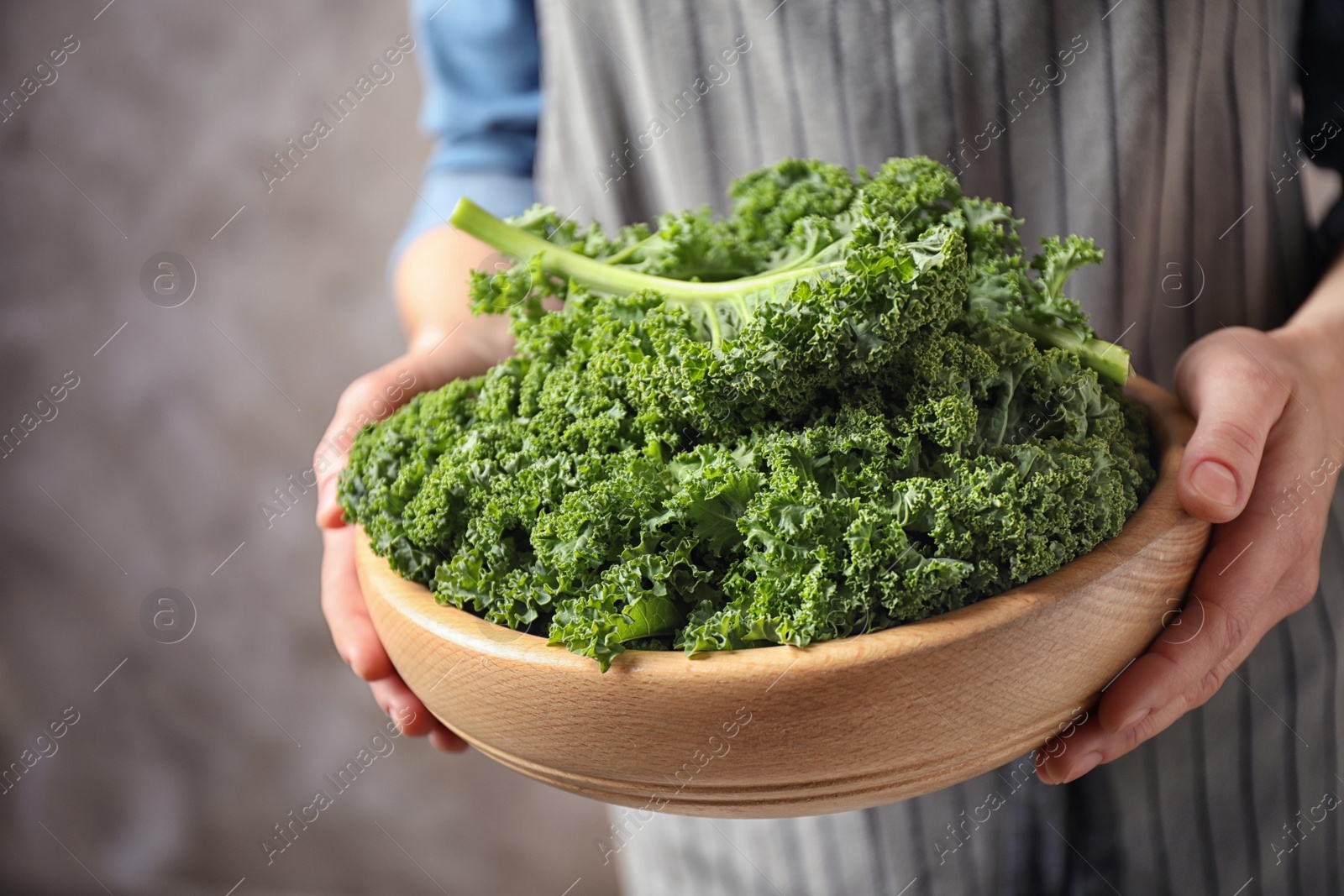 Photo of Woman holding fresh kale leaves on brown background, closeup