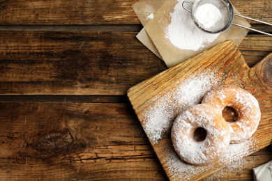 Photo of Delicious donuts with powdered sugar on wooden table, flat lay. Space for text