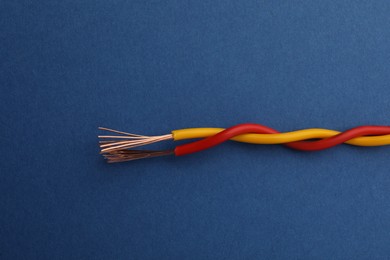 Photo of Two twisted electrical wires on blue background, closeup