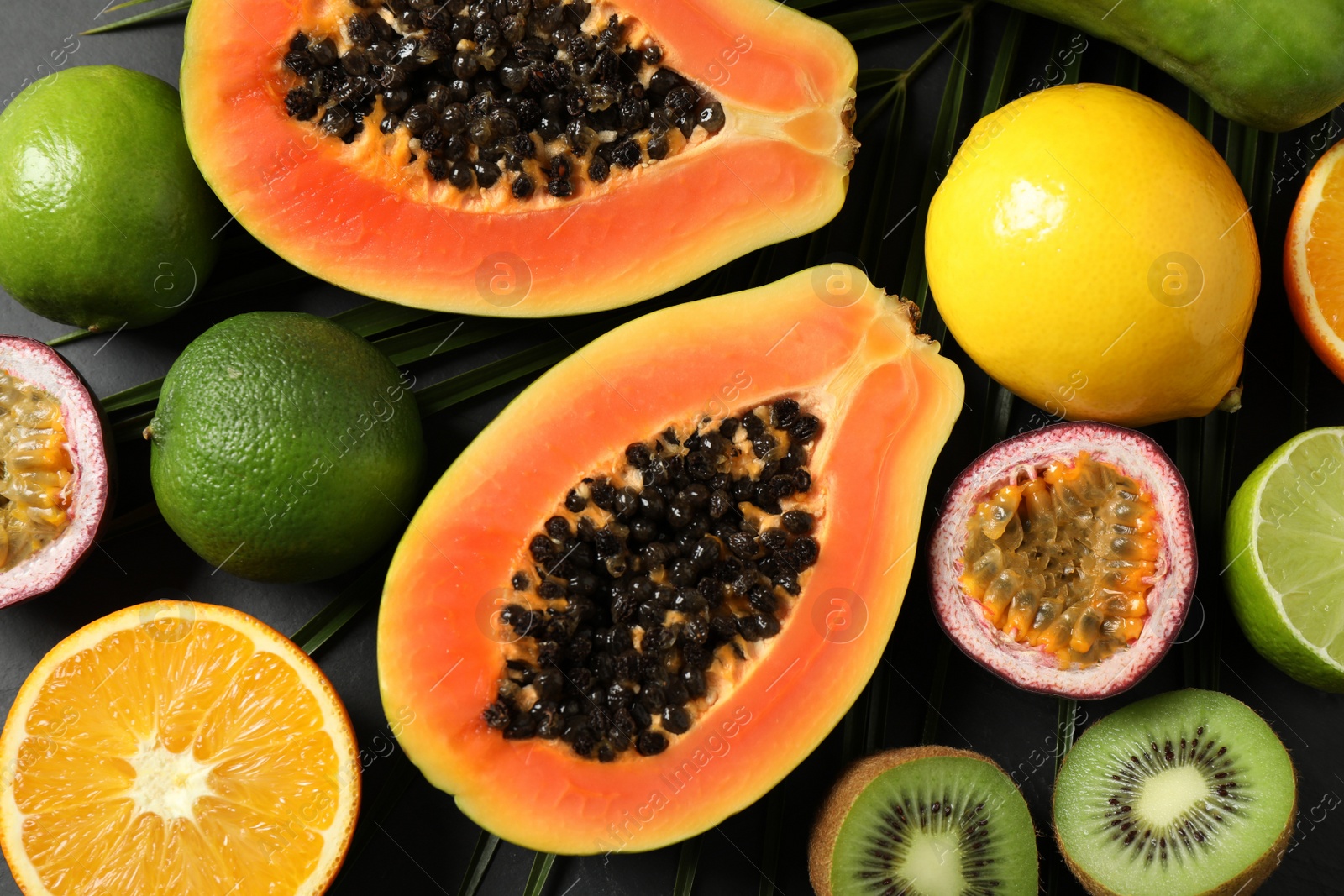 Photo of Fresh ripe papaya and other fruits on black table, flat lay