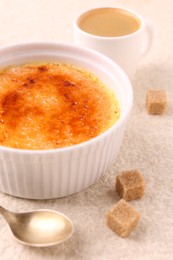 Photo of Delicious creme brulee in bowl, sugar cubes, coffee and spoon on light textured table, closeup