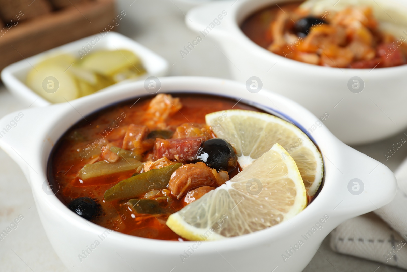 Photo of Meat solyanka soup with sausages, olives and vegetables on white table, closeup