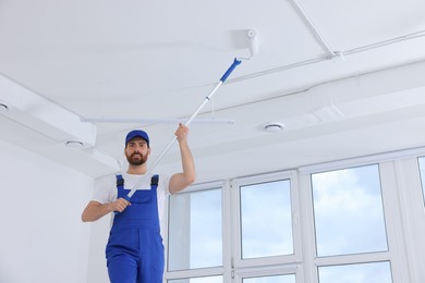 Handyman painting ceiling with roller in room