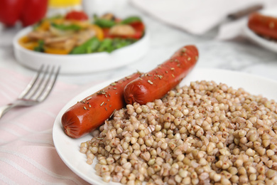 Photo of Tasty buckwheat porridge with sausages on table, closeup