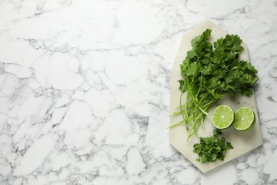 Photo of Fresh green cilantro and lime on white marble table, top view. Space for text