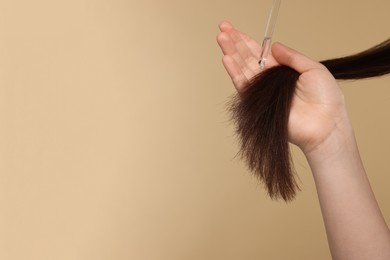 Woman applying essential oil onto hair on beige background, closeup and space for text