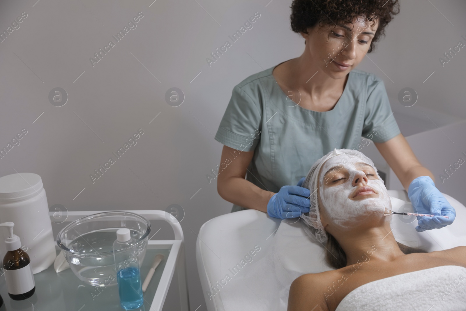 Photo of Cosmetologist applying mask on client's face in spa salon