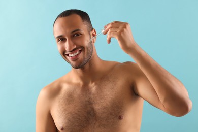 Handsome man applying cosmetic serum onto face on light blue background