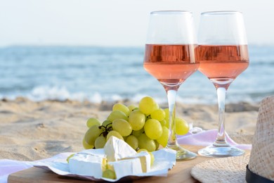 Photo of Glasses with rose wine and snacks on sandy seashore, closeup. Space for text