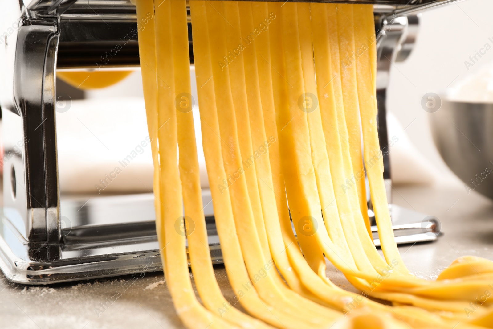 Photo of Pasta maker machine with dough on grey table, closeup