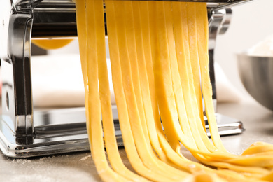 Photo of Pasta maker machine with dough on grey table, closeup