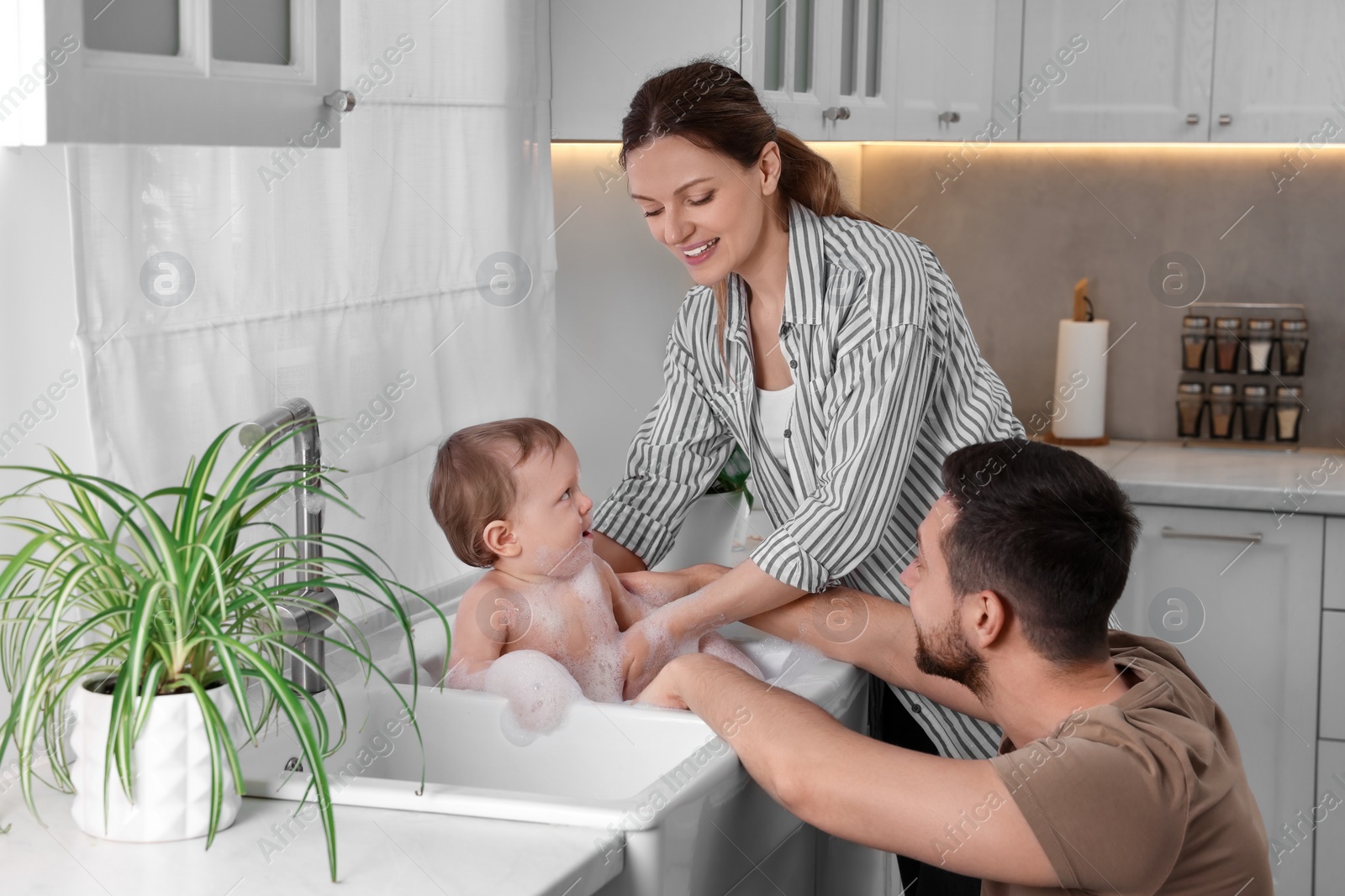 Photo of Father and mother washing their little baby in sink at home