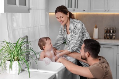 Father and mother washing their little baby in sink at home