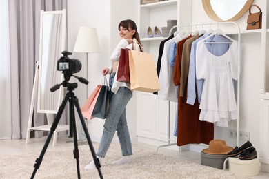 Smiling fashion blogger with shopping bags recording video at home